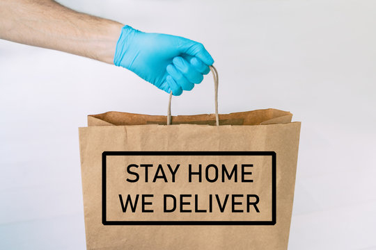 Home Delivery Food Grocery Delivered With Gloves For COVID-19 Quarantine From Coronavirus Social Distancing. Text Message Written : STAY HOME, WE DELIVER Man Giving Bag As Corona Virus Prevention.