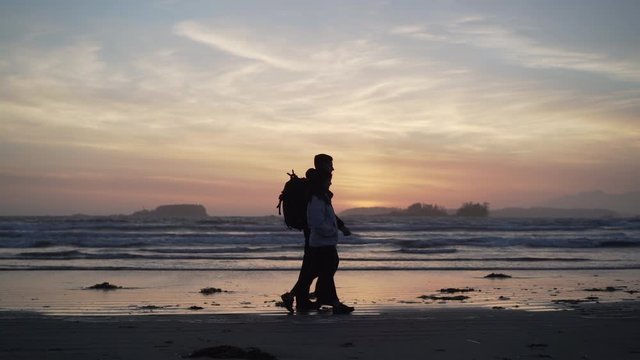 Couple walking on a beach at sunset in Tofino British Columbia, Canads