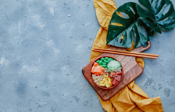 Hawaiian salmon poke bowl with rice, avocado, cucumber, carrot, chukka and sesame seeds on a blue background. top view