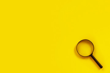 Black metal magnifier on a yellow paper background.