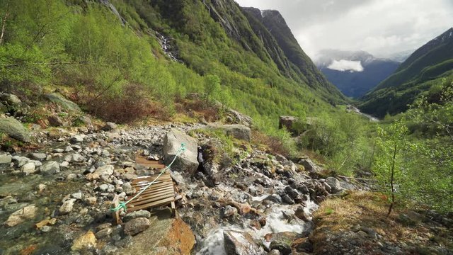 The foothills of the Buarbreen glacier in the Folgefonna national glacier park near Odda, Norway. A shallow stream rushing into the lush valley below. Dark mountains tower on the horizon