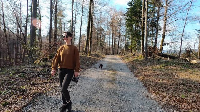 Young woman in casual clothes walking with small black dog in nature, footage with action camera
