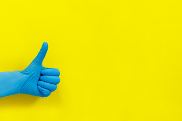 Hand in medical glove showing thumb up on yellow paper background.