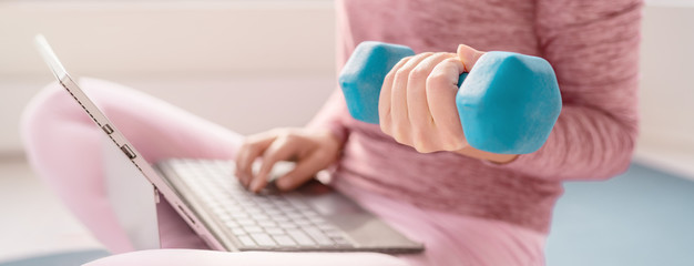 Woman using laptop at home watching fitness videos online workout class training with dumbbell...