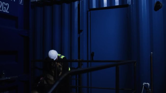 Wide shot as worker is caught sleeping on the job on nightshift at a shipping container yard while sitting beside a guard dog.