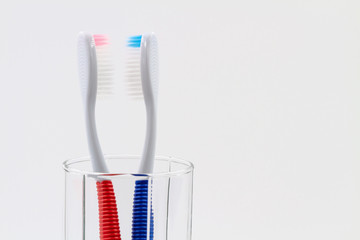 New red and blue plastic toothbrushes in the transparent glass. Bathroom wall. Light blue background. Closeup, copy space.