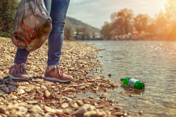 A woman stands on the Bank of the hand with a garbage bag, and a bottle lying in the water. The concept of the protection of the environment and earth Day. Tint and close up