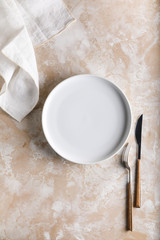 Creative background consisting of a ceramic empty plate, with a kitchen towel on a beige background.