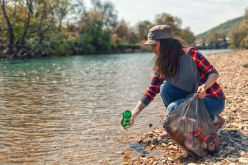 A woman volunteer pulls a bottle out of the water, during the event to clean the river Bank. Earth day and environmental improvement concept. Close up