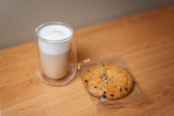 Cappuccino in a glass with double walls and bottom near the cookies on a wooden table.