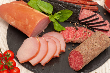 abstract background with smoked sausage with sauce, cherry tomatoes and basil on a black graphite board. top view