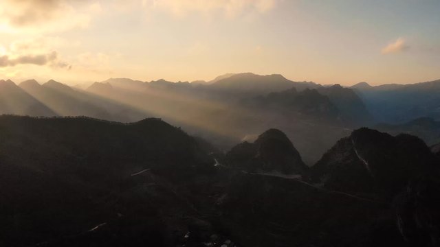 Aerial Pan Left With Golden Yellow Sunset With Sunbeams Across Mountain Peaks At Ha Giang, Vietnam 