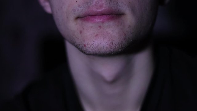 A young guy slowly exhales smoke in the night