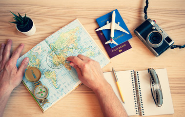 Fototapeta na wymiar Male hand holding a magnifying glass for planning trip with world map on the table. Travel concept. Sunglasses, Passports, Paper notebook, Compass, camera, toy plane. Adventure and travel concept
