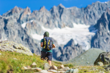 Fototapeta premium Woman with backpack hiking towards mountain top, scenic glacier and dramatic landscape summer fitness wellbeing selective focus rear view, freedom concept