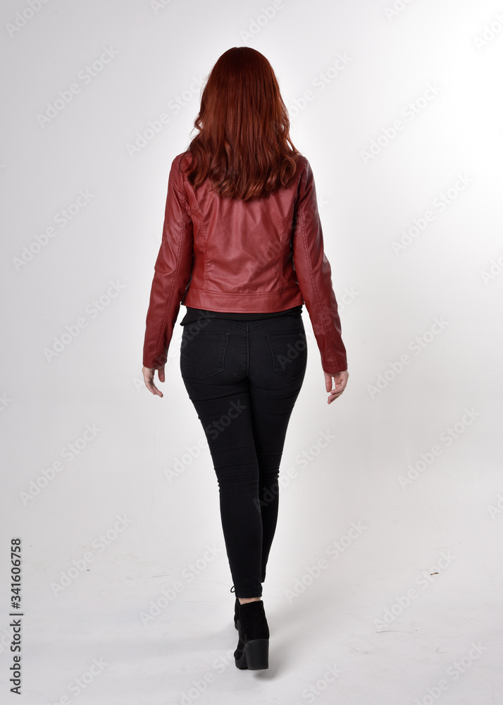 Canvas Prints Portrait of a pretty girl with red hair wearing black jeans and boots with leather jacket.  full length standing pose with back to the camera a studio background.