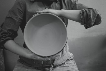 Potter holds round clay plate in his hands.