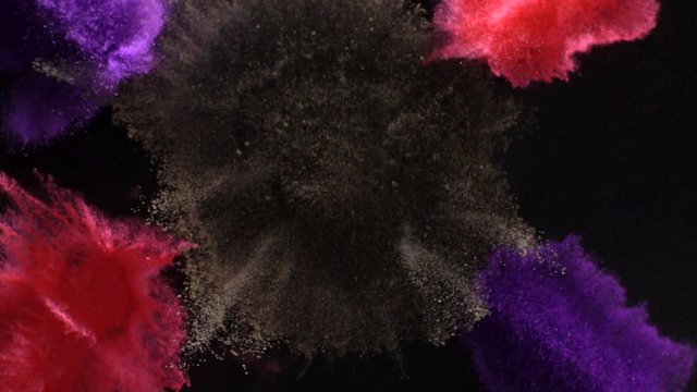In real slow motion, red, purple and black powder arranged in lines and circles explodes towards the camera. Top Shot