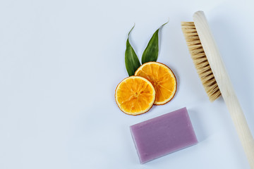 Slices of juicy orange, a body brush and handmade lavender soap on a pink background. The concept of home Spa.