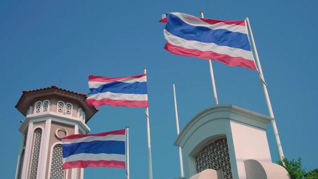 Vibrant Thai national flags  on the poles waving in the wind against chic clear blue sky and western tower decor background. Slow motion (half speed).