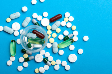 Many tablets and capsules are scattered and a dosage cup with tablets. Close-up, top view, on a blue background.