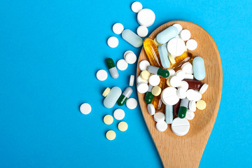 Many different pills and capsules of drugs in a wooden spoon. On a blue background. Close-up, top view. With free space for text.