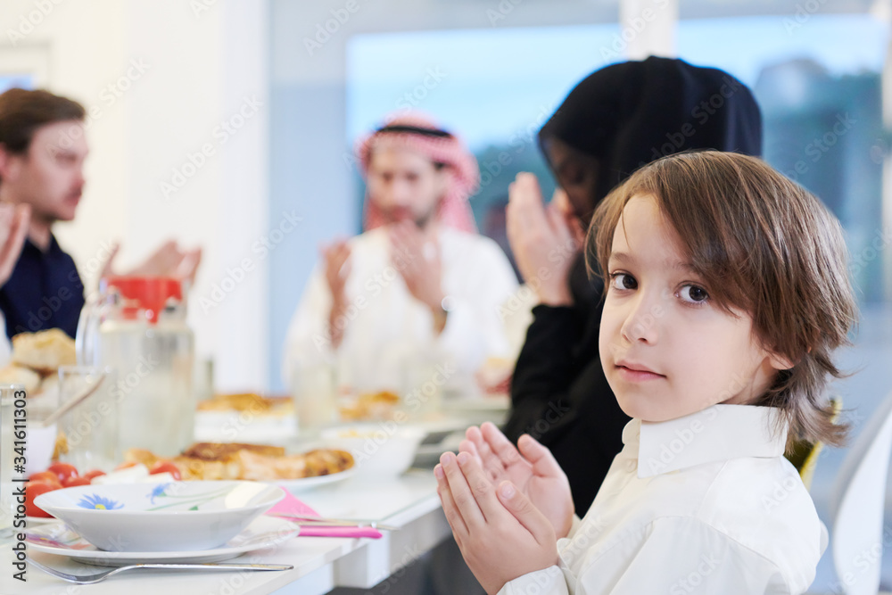 Wall mural little muslim boy praying with family before iftar dinner