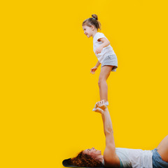 Acrobatic girl standing on mom's hands, happy and exhilarated over yellow