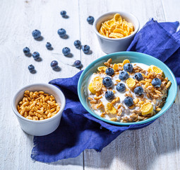 Yogurt, bowls with granola, blueberries, cornflakes and puffed rice on a white background. Healthy breakfast