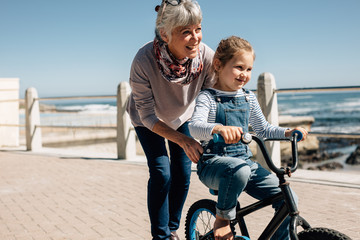 Fototapeta Senior woman helping her granddaughter learn to ride a bicycle obraz