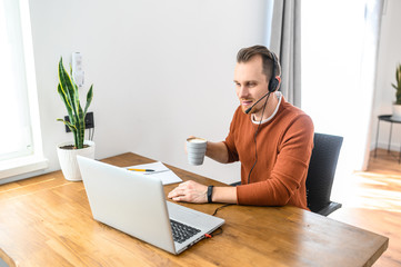 Work from home, home office. A young guy in casual clothes is using a headset for online...