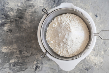 White wheat flour in a white bowl and dough sieve on a concrete background. Sift flour for yeast dough, oxygen enrichment. Top view. Copyspace for text