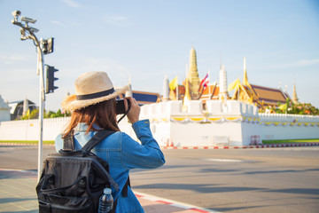 Obraz na płótnie Canvas back side Asian woman in jeans jacket and straw hat carrying a mini backpack taking a photo in front of Wat Phra Kaew one of Favorite place in Bangkok Thailand