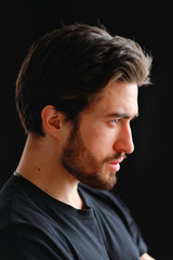 Fototapeta premium Close-up portrait of a young stylish man with a beard and dark hair in a black T-shirt 