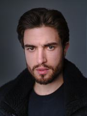 A large portrait of a stylish young man with a beard and dark hair in a black leather jacket