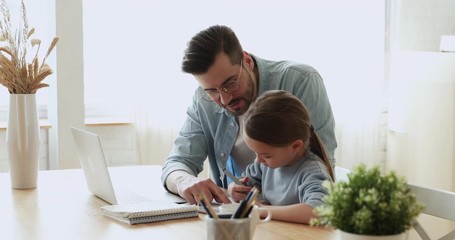 Dad helping cute small kid daughter doing homework at home. Young adult parent father or tutor explaining education teaching school girl pupil studying with daddy. Children remote education concept - Powered by Adobe