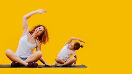 Mom and her little daughter doing doing side bends in easy pose over yellow © zzzdim