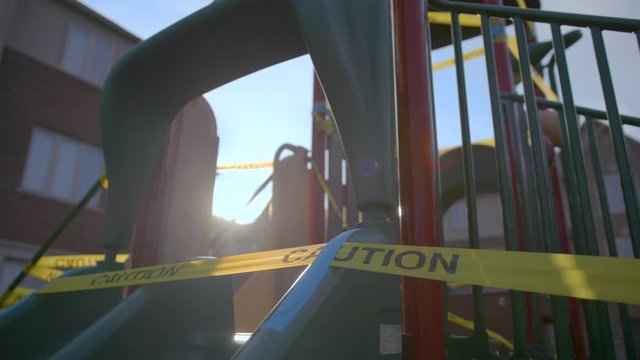 Close up of caution tape over a slide on a children's play structure with lens flare from the sun