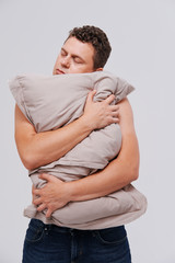Sleepy man with a naked torso hugs a pillow. 