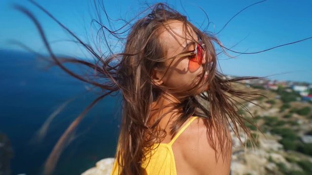 closeup clow motion portrait beautiful young smiling brunette woman with long wind blowing hair. girl wearing in orange sundress and sunglasses, wind flying hair to camera
