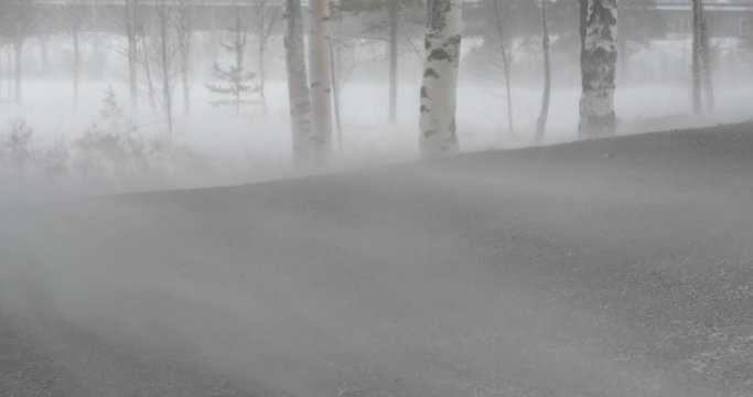 Handheld close up of gale force winds blowing across dry road during winter snowstorm