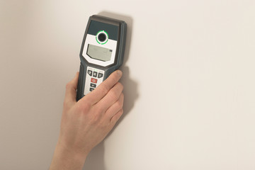 Man hand is scanning wall by cable detector to find a cable before drilling in.