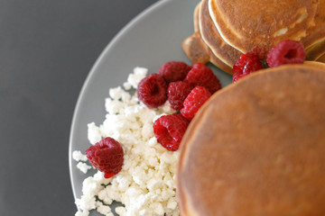 Pancakes with cottage cheese and raspberries on a gray plate, on a black background