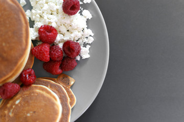 Pancakes with cottage cheese and raspberries on a gray plate, on a black background