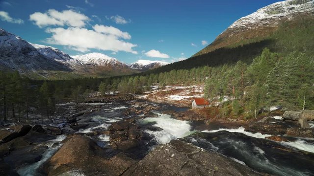 The canyon of the Gaular river ant the Likholefossen waterfall, Norway. Turbulent waters rush down to the valley, whirling and overflowing the banks. A small building - an old mill, is on the bank.