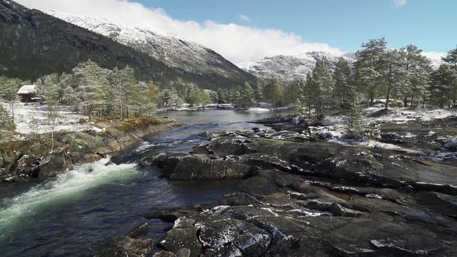 Gaula river near the Likholefossen waterfall. Powerful river carrying its' waters down to the valley. Pine forest stands on the riverbanks, wet stones glister in the sun.  Fresh snow on the ground.