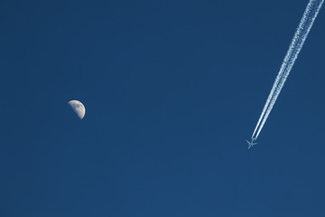 Blauer Himmel mit Halbmond links und Flugzeug mit kondenzstreifen rechts, Freiraum in der Mitte und oben