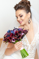Young beautiful bride holds a bouquet of dark purple callas.