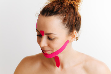 Amused giggling shy woman with pink anti-wrinkle tape on her face over white