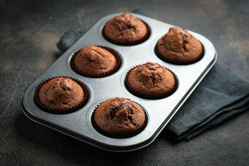 Various homemade muffins in a baking dish with berries, chocolate and mint on a dark background top view copy space.